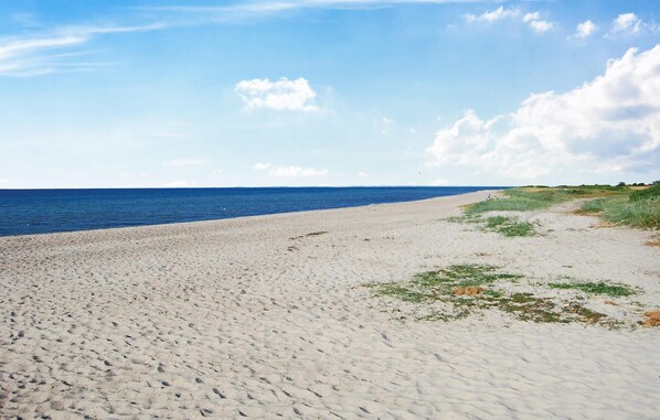 Una playa arenosa con vista despejada al océano y un área de césped con una persona sentada.