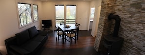 Ein Wohnzimmer mit einer Couch, einem Esstisch mit Stühlen, einem Fernseher und einem Kamin aus Stein.