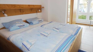 A bedroom with a wooden headboard, a bed with a blue and white striped bedspread, and a window with a view of the outside. - Windrose (EC) - At Rhododendron Park - Apartment Windrose 15 (Graal-Müritz)