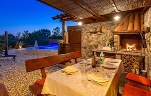 An outdoor dining area with a stone wall, a wood-fired oven, and a pool. - Beautiful home in Matulji (Matulji)