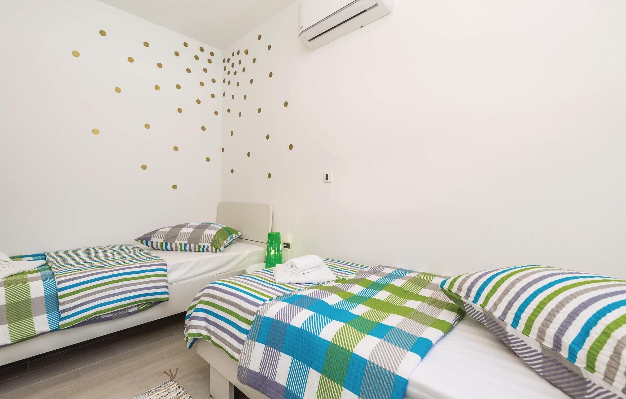 Hotellihuone, jossa on kaksi sänkyä, raidalliset vuodevaatteet, kultaisilla pisteillä koristeltu seinä ja vihreä pullo.