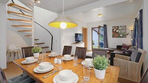 A dining area with a wooden table set for four, a staircase with wooden steps, and a television in the background.