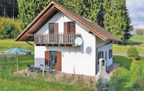 Ein zweistöckiges Haus mit Balkon, Schornstein und einer Terrasse mit Gartenmöbeln.
