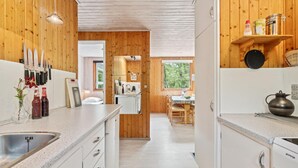 A modern kitchen with wooden walls, a central island, and a dining area with natural light. - 3 bedroom beautiful home in Nexø (Nexø)