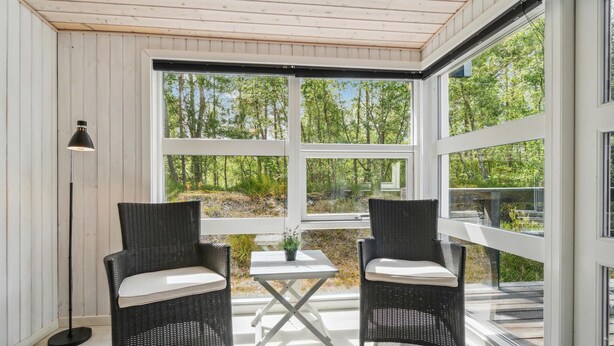 A room with two wicker chairs, a small table, and a floor lamp. Large windows offer a view of a forested area. - 3 bedroom beautiful home in Nexø (Nexø)