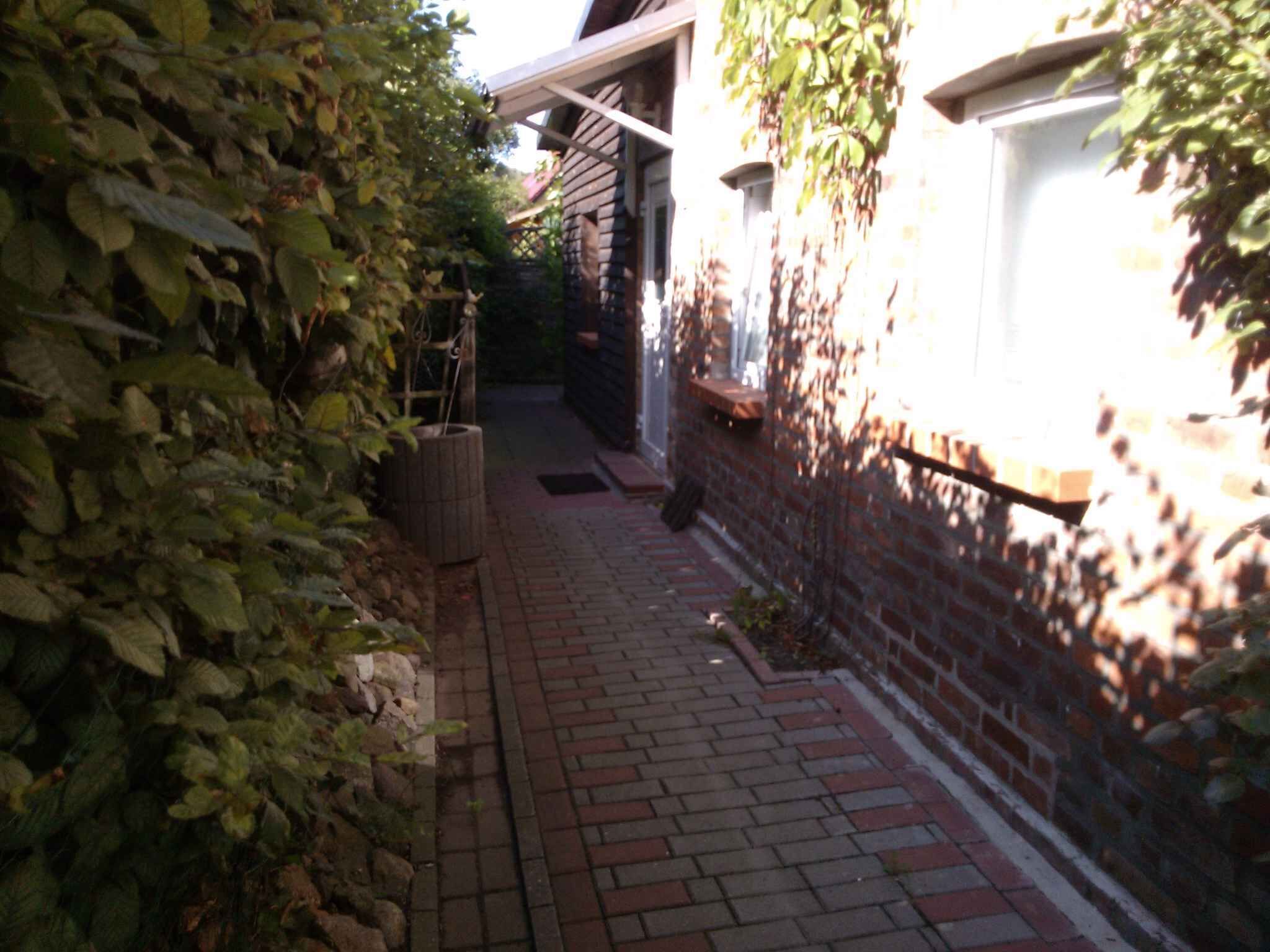 Un étroit sentier pavé de briques mène à un bâtiment à l’extérieur blanc et doté d’un mur en briques.