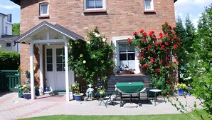 A two-story brick house with a covered porch, a front door, and a small window. There are potted plants and a green table outside. - Studio mit Terrasse und Garten (Putbus)