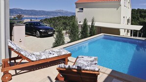 Une piscine avec des chaises longues, une voiture et un bâtiment doté d’un toit rouge.