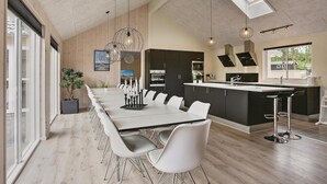 A modern kitchen with a central island, a dining area with a long table and chairs, and a large window providing natural light.