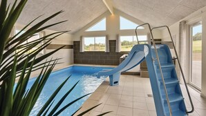 An indoor swimming pool with a blue slide, large windows, and a view of the outdoors.