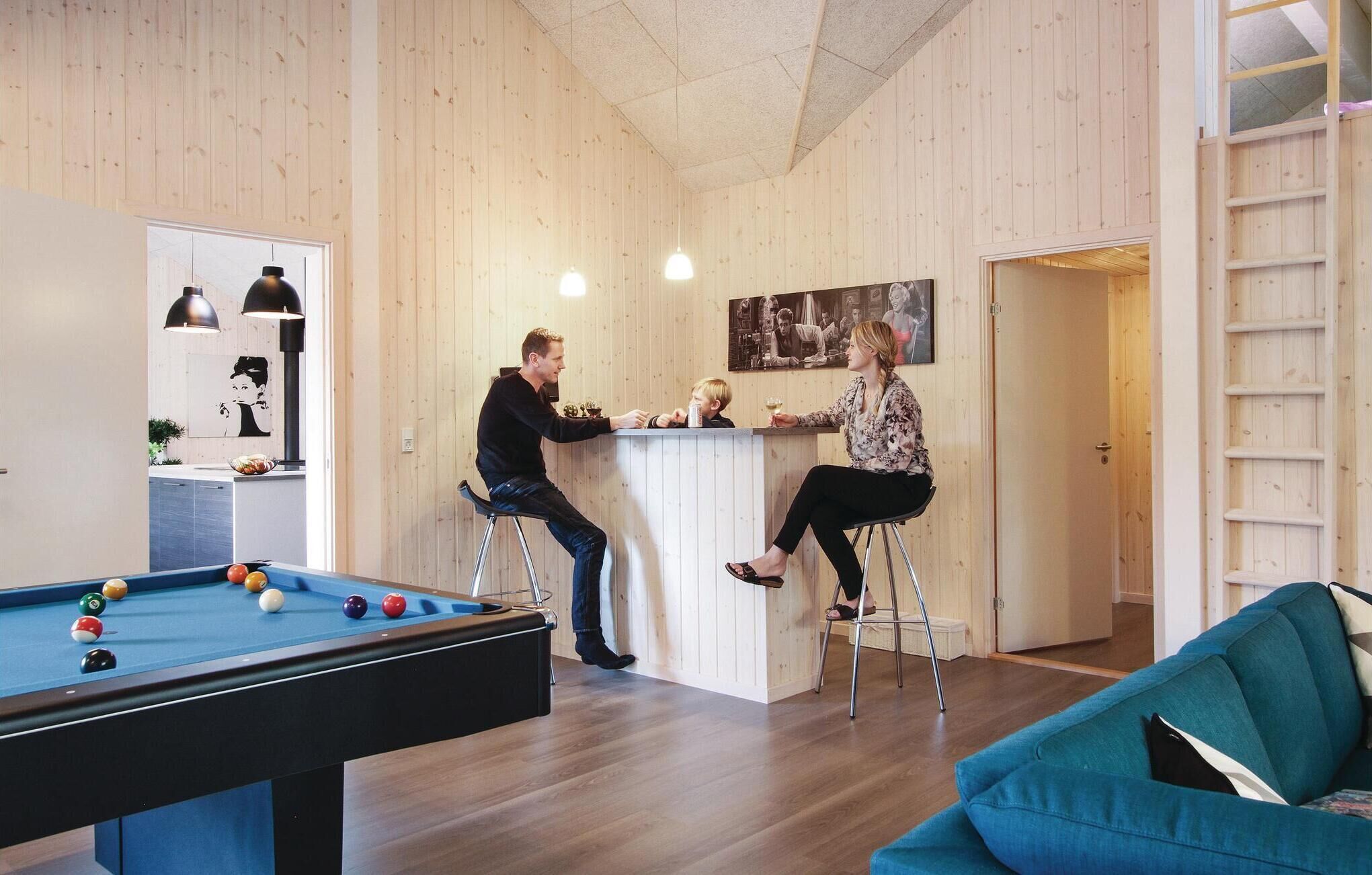 Een biljart met ballen, een bar en een blauwe bank in een kamer met houten lambrisering.