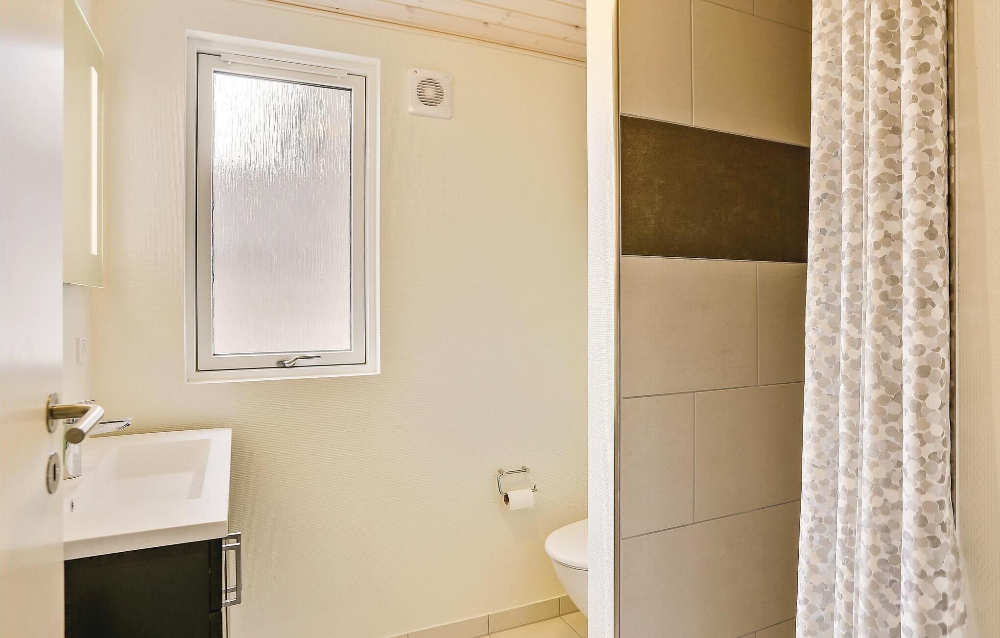 Une salle de bain comprenant des toilettes, une fenêtre et un espace douche.