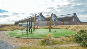 Ett utomhusgym med träningsredskap, en gräsyta och en byggnad med modern arkitektonisk design i bakgrunden.