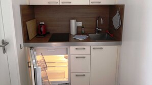 Una cucina compatta con lavandino, bollitore e un piccolo piano di lavoro.