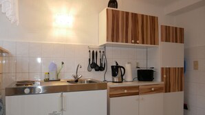 A kitchen with white cabinets, a stainless steel sink, and a built-in oven. There are wooden cabinets above the sink and a light fixture on the wall.