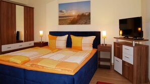 A bedroom with a large bed, a TV, a dresser, and a painting on the wall.