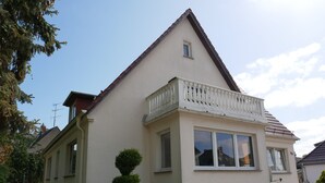 A two-story house with a balcony, a small window, and a statue in the front yard.