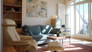 Un salon moderne comprenant un canapé, un fauteuil et un pouf, une bibliothèque et un grand tableau abstrait.