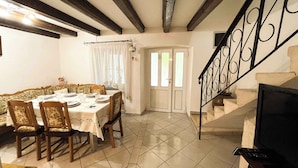 Un comedor con una mesa dispuesta para cuatro personas, una escalera con barandilla decorativa y un televisor sobre un mueble.