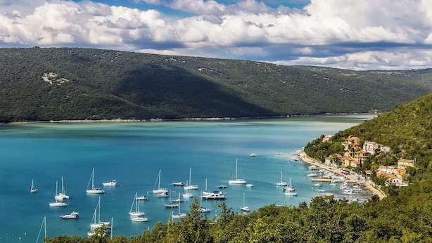 Un pueblo costero con barcos amarrados a la orilla, rodeado de colinas y un cielo despejado.