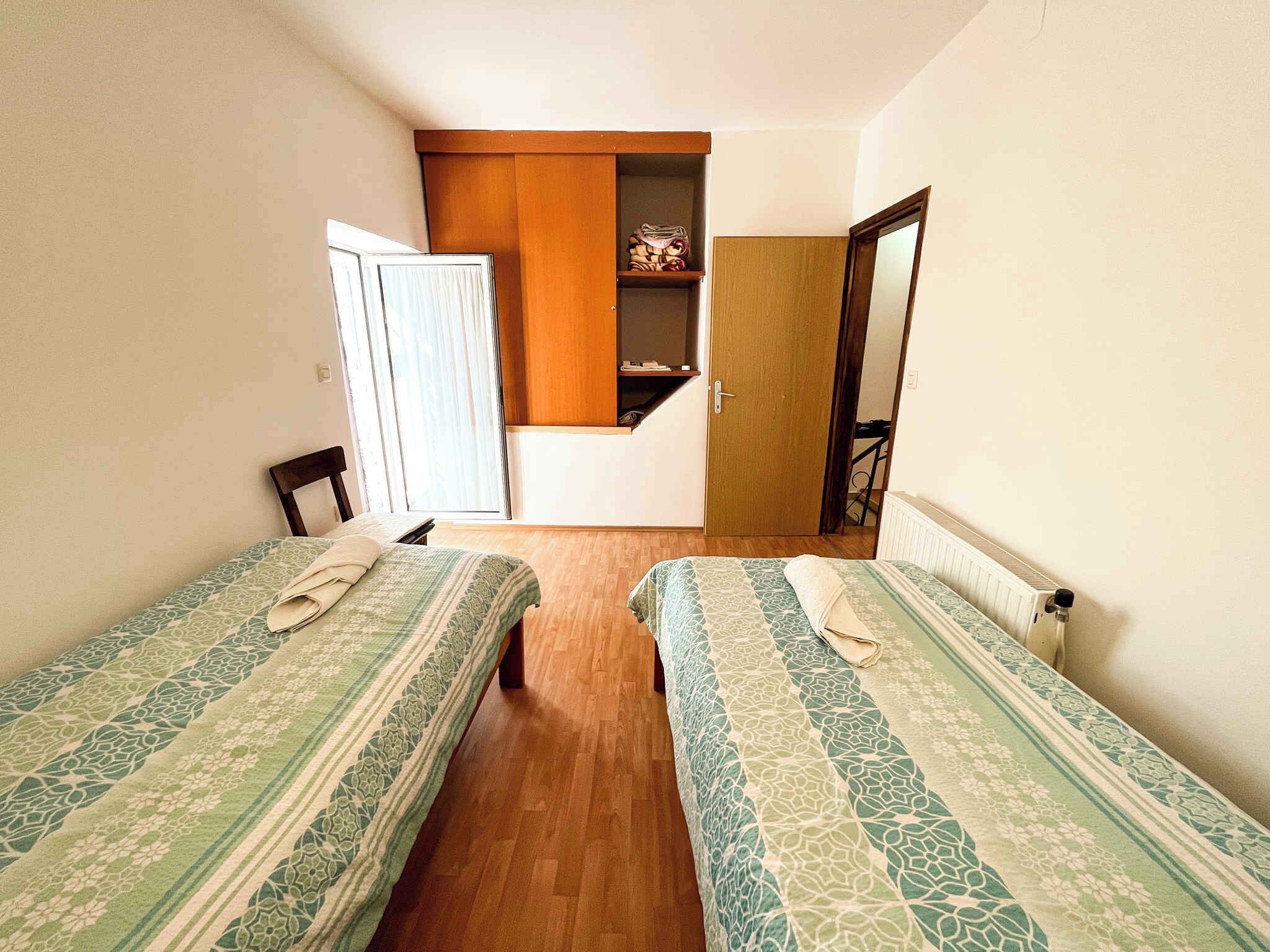 A small, cozy room with two single beds, a wooden wardrobe, and a small window.