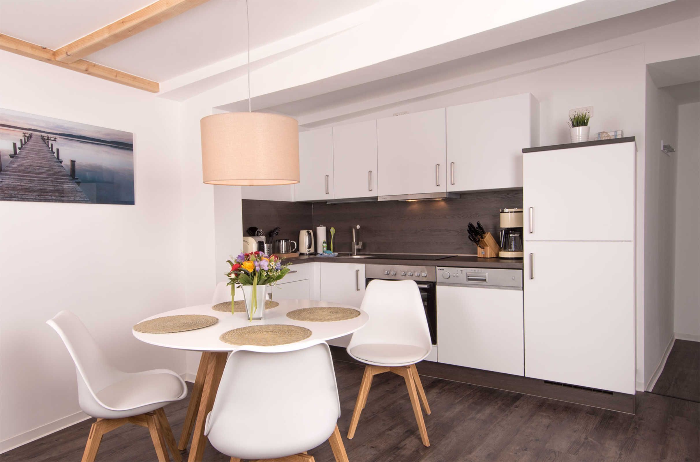 Una cocina moderna con armarios blancos, una mesa de comedor con sillas blancas y una lámpara colgante.