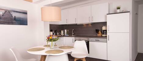 Una cocina moderna con armarios blancos, una mesa de comedor con sillas blancas y una lámpara colgante.