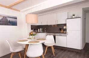 A modern kitchen with white cabinets, a dining table with white chairs, and a pendant light.