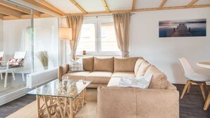 Una sala de estar moderna con una mesa de centro de vidrio, un sofá color beige y vistas a un muelle a través de una ventana.
