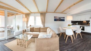 Una sala de estar moderna con una mesa de centro de vidrio, un sofá color beige y un comedor con una mesa redonda y sillas.