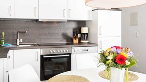 Una cocina moderna con armarios blancos, salpicadero de madera oscura, electrodomésticos de acero inoxidable y una zona de comedor con mesa y sillas.