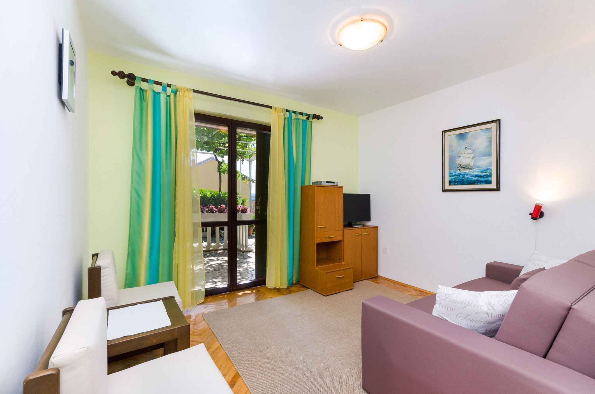 Un salón con sofá, mueble para televisión y puerta corredera de vidrio que da a un espacio exterior.