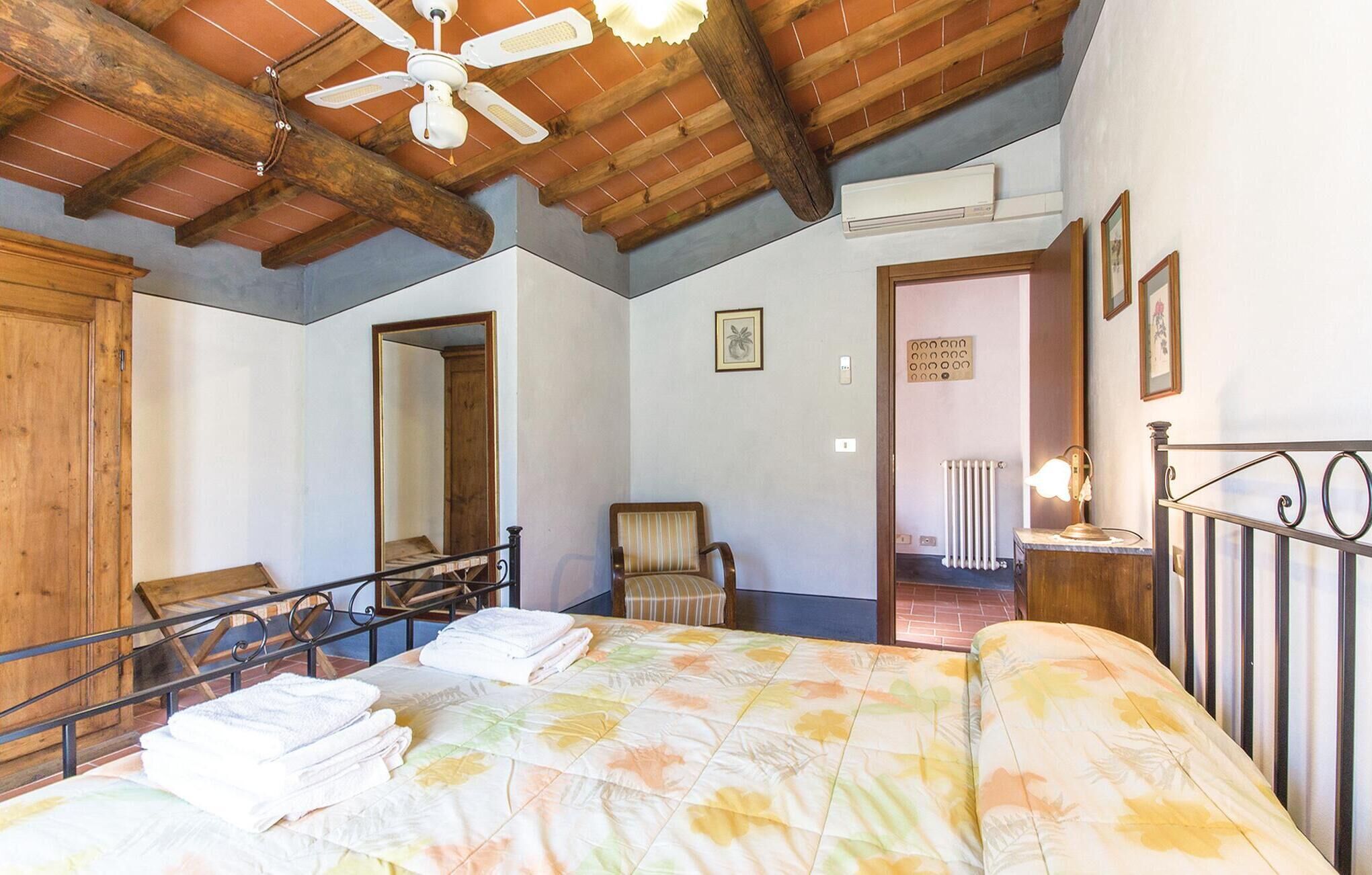 A bedroom with a bed, a chair, a desk, a mirror, and a ceiling fan.