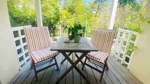 Une terrasse en bois avec une table et deux chaises à rayures, entourée de rampes blanches et de verdure.