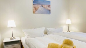 Une chambre d’hôtel avec deux lits, du linge de lit blanc, deux lampes de chevet, une table de chevet, une petite armoire et un tableau au mur.
