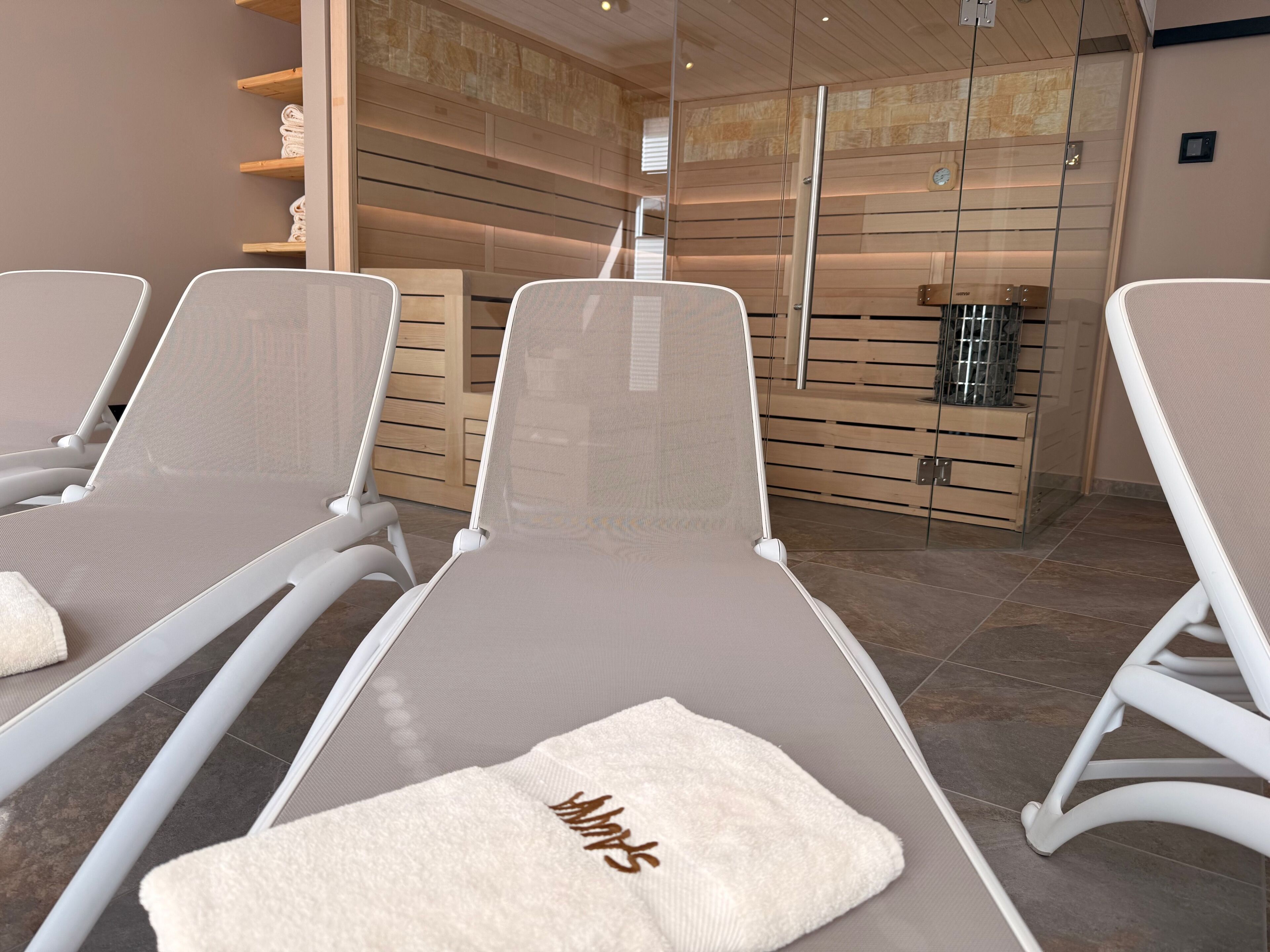 Una moderna stanza spa con poltrone reclinabili, una parete in legno e una porta in vetro che dà su un’area doccia.
