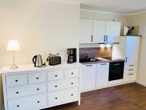 Eine kompakte Küche mit weißen Schränken, einer Kaffeemaschine, einem Toaster und einem Wasserkocher auf der Arbeitsfläche.