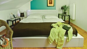 A neatly made bed with a white headboard, a green blanket, and a green jacket on the footboard. There is a wicker chair with a colorful scarf, a small table with a lamp, and a framed picture on the wall. - Stunning home in Pinnow with WiFi (Pinnow)
