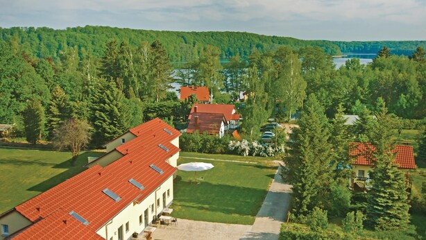 A large building with multiple red-tiled roofs, surrounded by lush greenery and a lake in the background. - Stunning home in Pinnow with WiFi (Pinnow)
