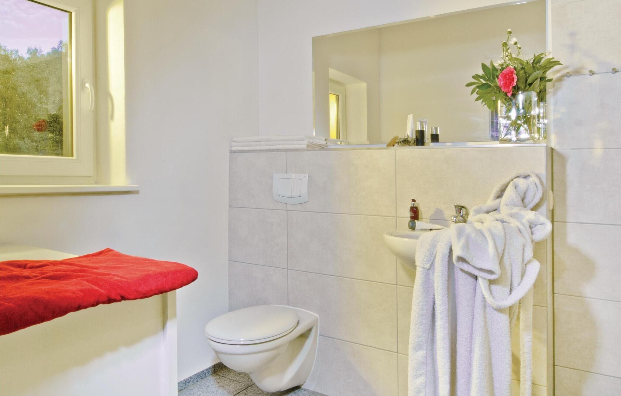 A bathroom with a toilet, a sink with a mirror, a towel rack with a towel, and a red bath mat.