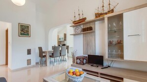 Una sala de estar moderna con comedor, televisor y un modelo de barco de madera en la estantería.