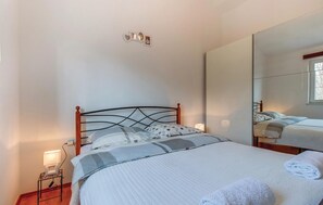 Een slaapkamer met een bed, een bedlamp, een spiegel en een aan de muur bevestigd fotolijstje.