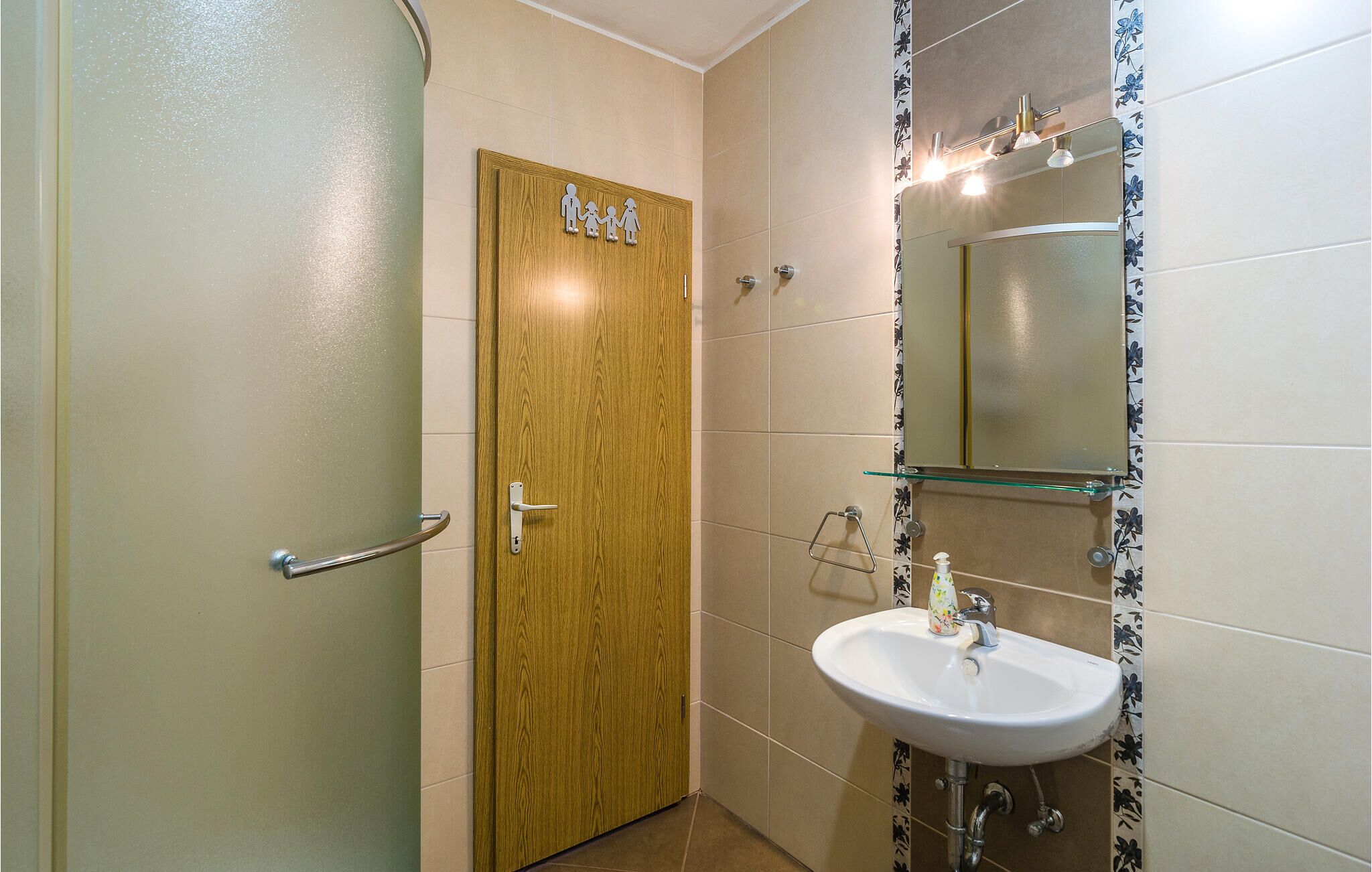 A bathroom with a wooden door, a glass shower enclosure, and a white sink with a mirror above it.