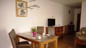 Een eetruimte met een houten tafel, stoelen en een potplant. Een flatscreen televisie hangt aan de muur.