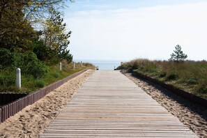 A wooden boardwalk leading to a beach, surrounded by vegetation and a clear sky.