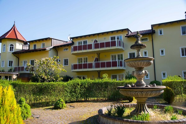 A courtyard with a fountain, a yellow building with balconies, and a red-roofed tower.