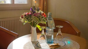 A dining table with a lace tablecloth, a vase with flowers, a bottle of Güstrower Gourmet, and a glass.