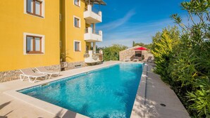 Una piscina con sillones de descanso, un muro de piedra y un edificio amarillo con balcones.