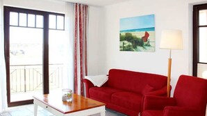 Een woonkamer met een rode bank, een houten salontafel, een lamp en een schilderij aan de muur.