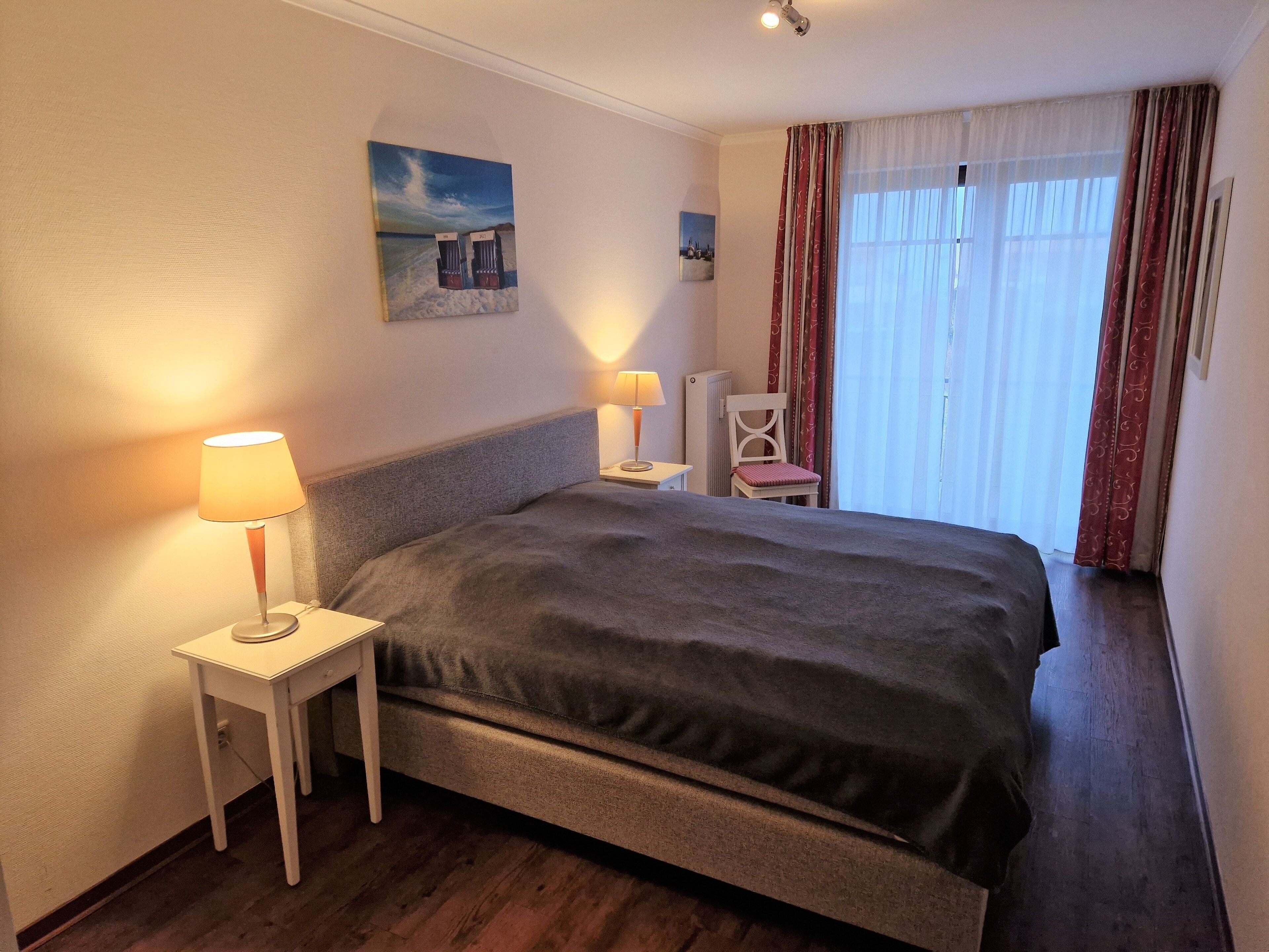Hotellihuone, jossa on suuri sänky, kaksi yöpöytää, tuoli ja ikkuna, jossa on verhot.